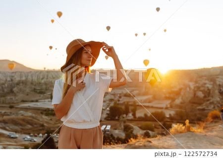 Woman stands on mountain with flying air balloons on background. Tourist Turkish region Cappadocia. 122572734