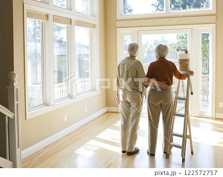 An older couple in work clothes standing in a sunlit room, admiring their progress in painting the walls 122572757