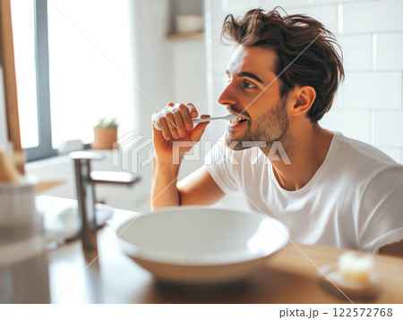 Young man brushing his teeth in a bright modern bathroom with natural light 122572768