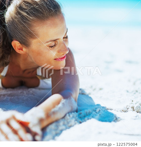 Relaxed young woman in swimsuit laying on beach Relaxed young woman in swimsuit laying on beach 122575004