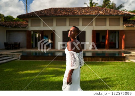 Ambiguous gender fluid person in white bridal dress by villa. Wedding vibe in tropical garden LGBTQ inclusive scene, representing modern love. Diverse, elegant, non-traditional marriage setting. Ambiguous gender fluid person in white bridal dress by villa. Wedding vibe in tropical garden LGBTQ inclusive scene, representing modern love. Diverse, elegant, non-traditional marriage setting. 122575099