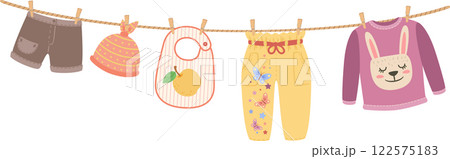 Baby clothes are hanging on a clothesline including shorts, a hat, a bib, pants and a sweater with a cute bunny design, suggesting laundry and childcare 122575183