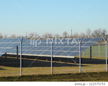 solar battery in the structure of energy storage station behind transparent fence on sunny day, collection of solar energy by large panels on farm in field solar battery in the structure of energy storage station behind transparent fence on sunny day, collection of solar energy by large panels on farm in field 122575735