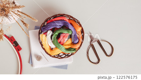Basket with colored floss and canvas for embroidery on a gray top view web banner 122576175