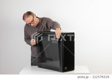 Man removing  tempered-glass left panel  from  PC case, empty big tower, chassis. 122576529