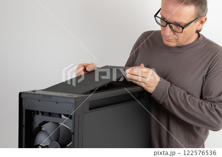 Man installing  top panel with dust filter to  PC case, empty big tower, chassis. Under top panel is place for 420 mm radiator for AIO cooling 122576536