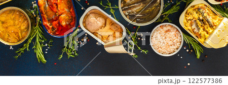 A top view of open tin cans with canned salmon, mackerel, sprat, sardine, tuna, herring, and fish pate, surrounded by spices and herbs on a blue background, banner A top view of open tin cans with canned salmon, mackerel, sprat, sardine, tuna, herring, and fish pate, surrounded by spices and herbs on a blue background, banner 122577386