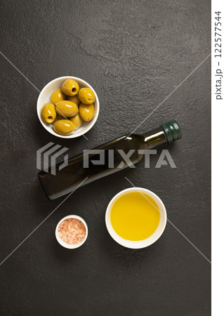 Olives and olive oil in bowl with bottle of olive oil on dark background. Mockup for package. Copy space. Olives and olive oil in bowl with bottle of olive oil on dark background. Mockup for package. Copy space. 122577544