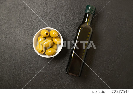 Olives and olive oil in bowl with bottle of olive oil on dark background. Mockup for package. Copy space. Olives and olive oil in bowl with bottle of olive oil on dark background. Mockup for package. Copy space. 122577545