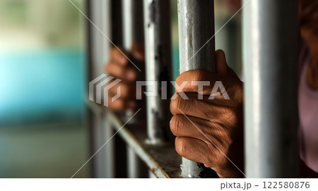 Individual holding onto prison bars in a confined space during the day 122580876
