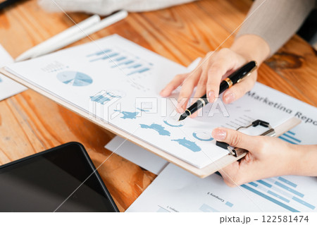 Close-up of hands reviewing marketing report with charts and graphs on a clipboard, highlighting business analysis. 122581474