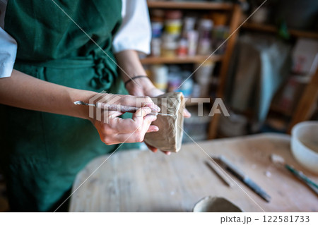 Potter hand carving pattern on clay bowl with knife in workshop. Manual labor, creative ceramic work Potter hand carving pattern on clay bowl with knife in workshop. Manual labor, creative ceramic work 122581733