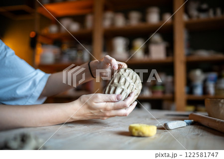 Molding craft ceramics: table in pottery studio with female artist shaping wet clay for potter bow Molding craft ceramics: table in pottery studio with female artist shaping wet clay for potter bow 122581747