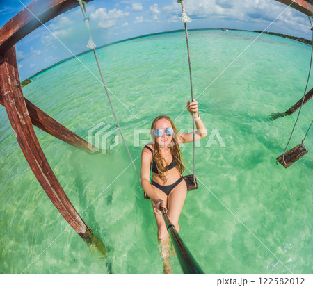 Woman standing in the crystal-clear waters of Lake Bacalar, Mexico, enjoying the serene beauty of the landscape. Tranquil moment in nature, outdoor escape, and relaxation concept 122582012
