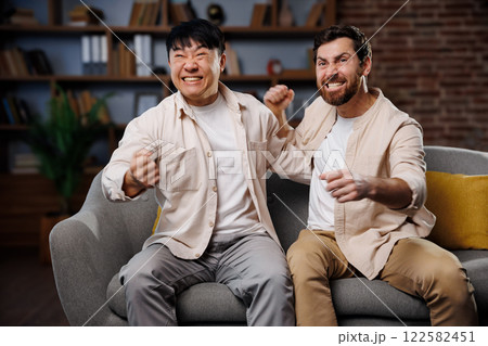 fans watching game, celebrating victory, Excited friends watching TV, Two friends joyfully cheer together on a couch during a thrilling moment of a sports event, showcasing their excitement and 122582451
