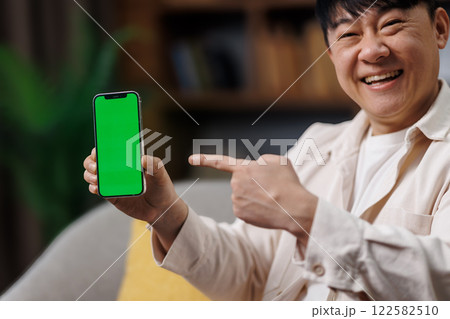 Amazing Useful App, Great Mobile Offer, Mobile Advertisement, Excited man, cheerful man points at a smartphone with a green screen, sitting comfortably in his living room decorated with plants Amazing Useful App, Great Mobile Offer, Mobile Advertisement, Excited man, cheerful man points at a smartphone with a green screen, sitting comfortably in his living room decorated with plants 122582510