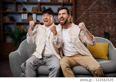 fans watching game, celebrating victory, Excited friends watching TV, Two friends express their excitement while watching a thrilling event in a cozy living room, cheering with joyful energy and fans watching game, celebrating victory, Excited friends watching TV, Two friends express their excitement while watching a thrilling event in a cozy living room, cheering with joyful energy and 122582529
