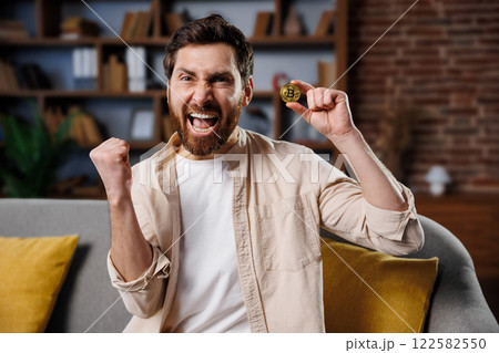 Portrait mature businessman, gold bitcoin coin, shows cryptocurrency coin, man with a beard is celebrating joyfully while holding a cryptocurrency token. He pumps his fist in the air, expressing Portrait mature businessman, gold bitcoin coin, shows cryptocurrency coin, man with a beard is celebrating joyfully while holding a cryptocurrency token. He pumps his fist in the air, expressing 122582550