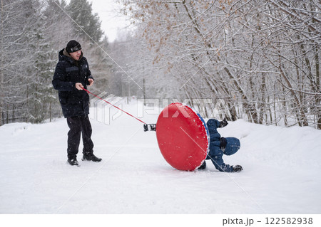 a child flips over from snow tubing while riding with his dad against the backdrop of a winter forest. Dangerous skiing in winter. Children's injuries during winter sports a child flips over from snow tubing while riding with his dad against the backdrop of a winter forest. Dangerous skiing in winter. Children's injuries during winter sports 122582938