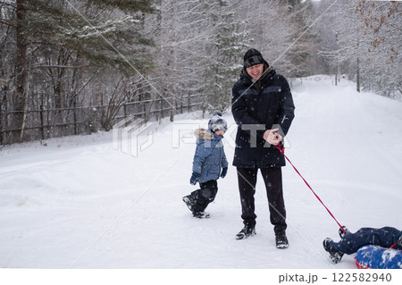 dad in winter jacket rides child on snow tubing around himself, against the background of snowfall and forest in winter. Dangerous and fun games of dad and son in winter dad in winter jacket rides child on snow tubing around himself, against the background of snowfall and forest in winter. Dangerous and fun games of dad and son in winter 122582940