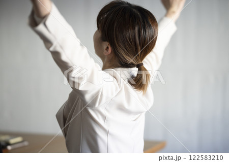 ノートパソコンの前で伸びをする女性 122583210