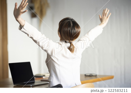 ノートパソコンの前で伸びをする女性 122583211