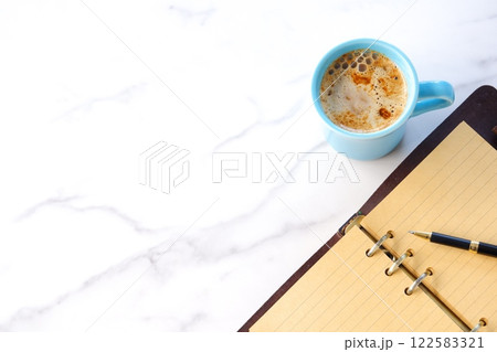 ミルクをたっぷり入れたコーヒー、カフェ・ラッテを飲みながら、システム手帳でデスクワーク中のイメージ ミルクをたっぷり入れたコーヒー、カフェ・ラッテを飲みながら、システム手帳でデスクワーク中のイメージ 122583321