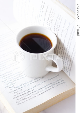 ページを開いたペーパーバック(洋書)とコーヒーの入ったコーヒーカップで、コーヒーを飲みながら読書中 ページを開いたペーパーバック(洋書)とコーヒーの入ったコーヒーカップで、コーヒーを飲みながら読書中 122583397