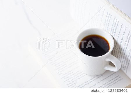 ページを開いたペーパーバック(洋書)とコーヒーの入ったコーヒーカップで、コーヒーを飲みながら読書中 ページを開いたペーパーバック(洋書)とコーヒーの入ったコーヒーカップで、コーヒーを飲みながら読書中 122583401