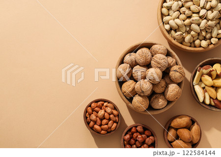 Various nuts in wooden bowls on a beige background 122584144