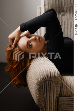 Elegant redhead woman with long hair leaning back in chair looking at camera Elegant redhead woman with long hair leaning back in chair looking at camera 122586067
