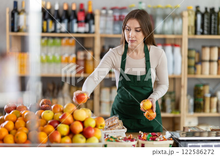 Girl put apples in window, replenishes fruit stocks on counter, correct appearance of product display 122586272