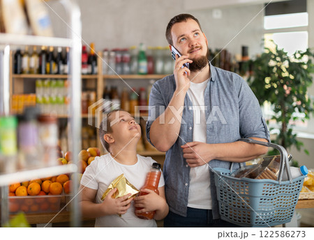 Young man talking on phone while grocery shopping with teenage son 122586273