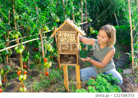 Portrait of happy girl next to hotel for insects in of wooden birdhouse in garden 122586355