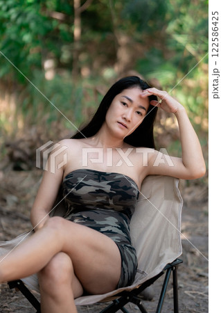 Portrait of sexy asian woman in a military print strapless dress, camping in the forest concept. Portrait of sexy asian woman in a military print strapless dress, camping in the forest concept. 122586425