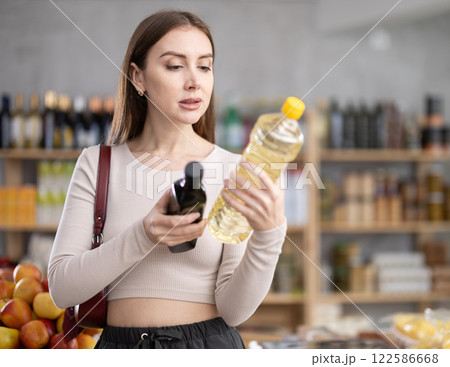 Young woman choosing olive and sunflower oil in grocery 122586668