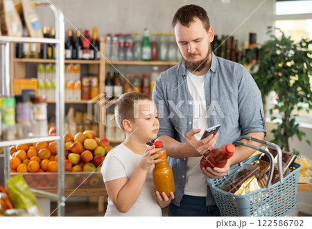 Man with preteen son scanning barcode on juice bottle with phone in store 122586702