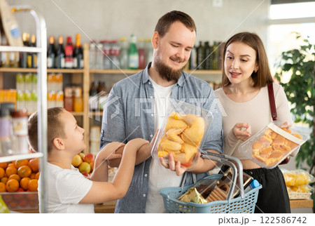 Family shopping - father, mother and son choose chicken thighs together in supermarket 122586742