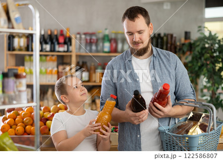 Man with son hold packages plastic bottle and choose consider fruit juice in store Man with son hold packages plastic bottle and choose consider fruit juice in store 122586807