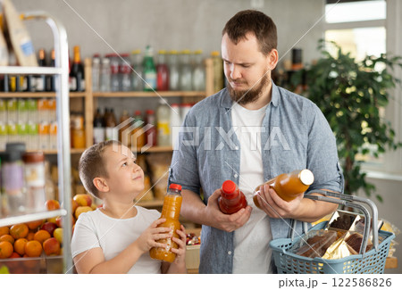 Man with son hold packages plastic bottle and choose consider fruit juice in store Man with son hold packages plastic bottle and choose consider fruit juice in store 122586826
