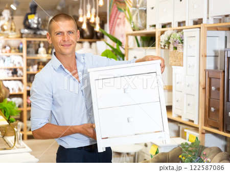 Man holding wooden chest of drawers at store 122587086
