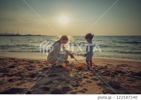 happy toddler baby girl playing sand toy with mother on sea beach at sunset in Pattaya, Thailand happy toddler baby girl playing sand toy with mother on sea beach at sunset in Pattaya, Thailand 122587240