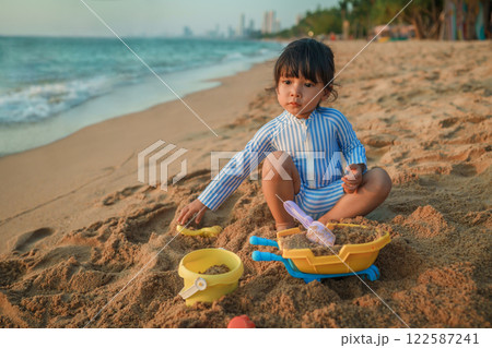 happy toddler baby girl playing sand toy on sea beach in Pattaya, Thailand happy toddler baby girl playing sand toy on sea beach in Pattaya, Thailand 122587241