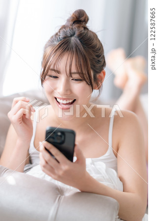 自宅でスマホを片手に微笑む若い女性 自宅でスマホを片手に微笑む若い女性 122587665