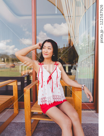 Beautiful and sexy asian woman posing on a wooden chair, chest revealing white shirt, red skirt. Beautiful and sexy asian woman posing on a wooden chair, chest revealing white shirt, red skirt. 122587926