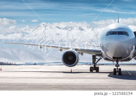 Front view of the white wide body passenger airplane at the airport on the background of high snow capped mountains Front view of the white wide body passenger airplane at the airport on the background of high snow capped mountains 122588154