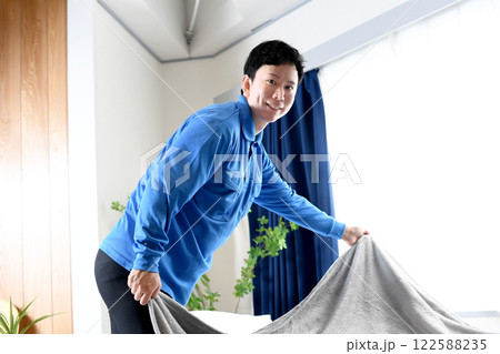 ベッドメイキングする作業着のアジア人男性 ベッドメイキングする作業着のアジア人男性 122588235