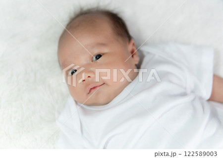 Close-up of a happy smiling baby on a white cotton bed in a bright bedroom. Close-up of a happy smiling baby on a white cotton bed in a bright bedroom. 122589003