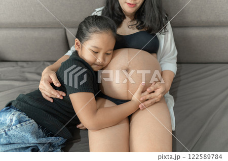 Pregnant woman and eldest daughter A cute girl leans her ear against her mother's belly. Pregnant woman and eldest daughter A cute girl leans her ear against her mother's belly. 122589784