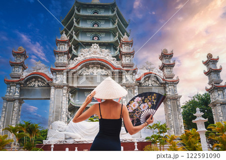 back of a female tourist in a Vietnamese Non La hat at Da Nang pagoda in Vietnam. Travel and tourism in Asia 122591090